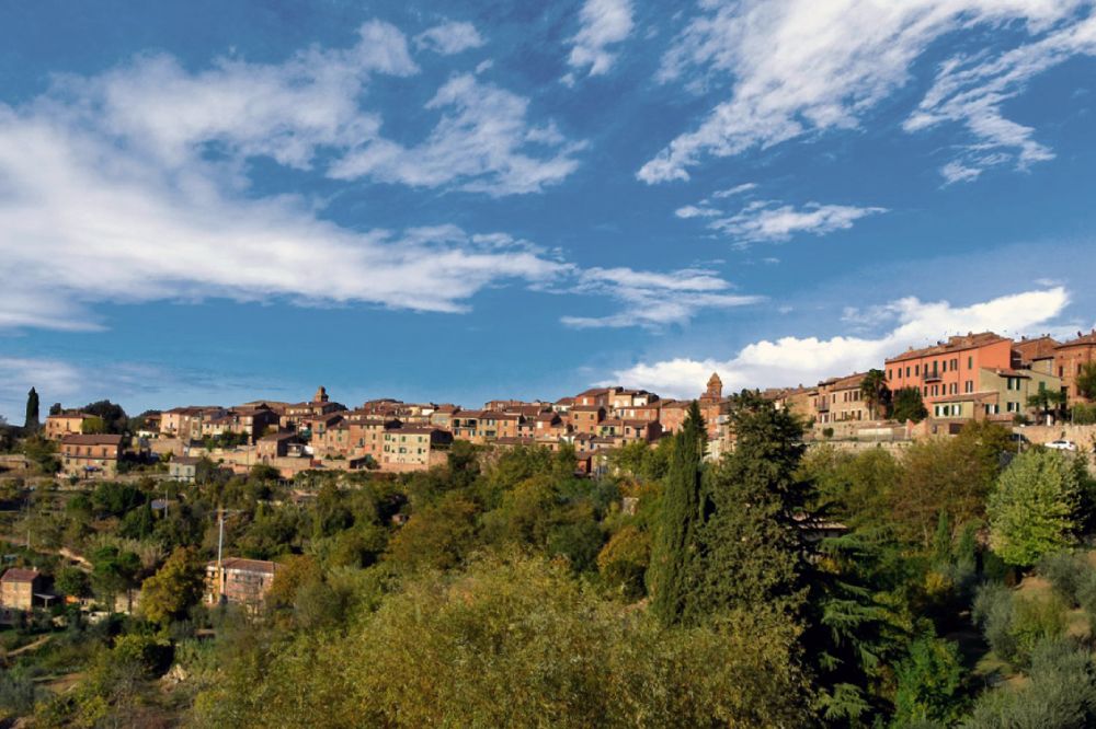 View of Città della Pieve, a medieval hilltop town with brick buildings, surrounded by lush vegetation.